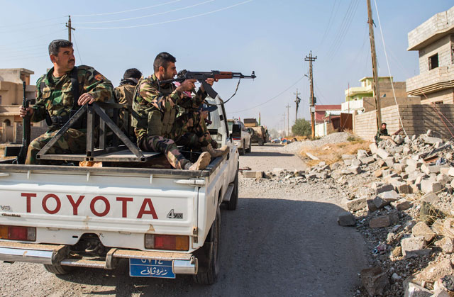 A peshmerga soldier returns fire as his convoy drives through an area exposed to a sniper fire on Monday, as the Iraqi Kurdish forces pushed deeper into the town of Bashiqa during street battles against Daesh militants (AFP photo)