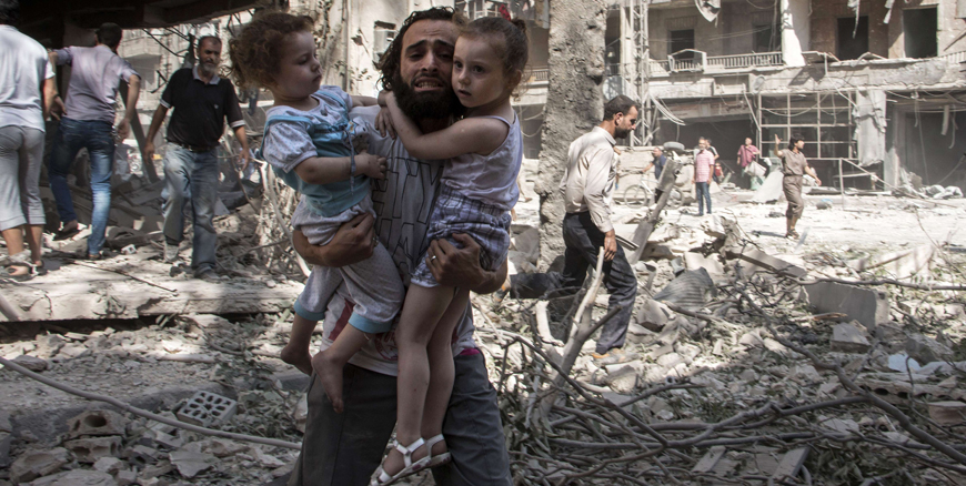 A Syrian man carries his two girls as he walks across the rubble following a barrel bomb attack on the rebel-held neighbourhood of Al Kalasa in the northern Syrian city of Aleppo on Thursday (AFP photo)