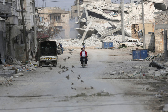 Birds fly near men riding a motorcycle through a damaged neighbourhood in the northern Syrian town of Al Bab, Syria, on Saturday (Reuters photo)
