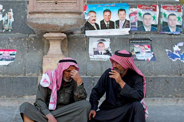 Syrian men sit in front of campaign posters of parliamentary candidates in the Marjeh Square in Damascus, Syria, on Monday (AP photo)