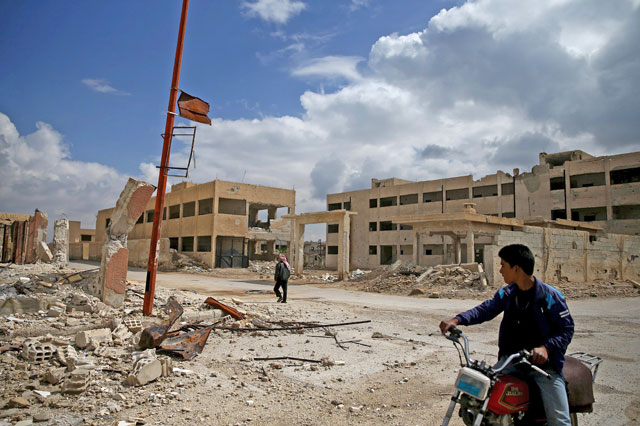 A man rides on a motorbike as another one walks past damaged buildings in the rebel-controlled area of Al Nashabiya town in Eastern Ghouta, Syria, on Thursday (Reuters photo)