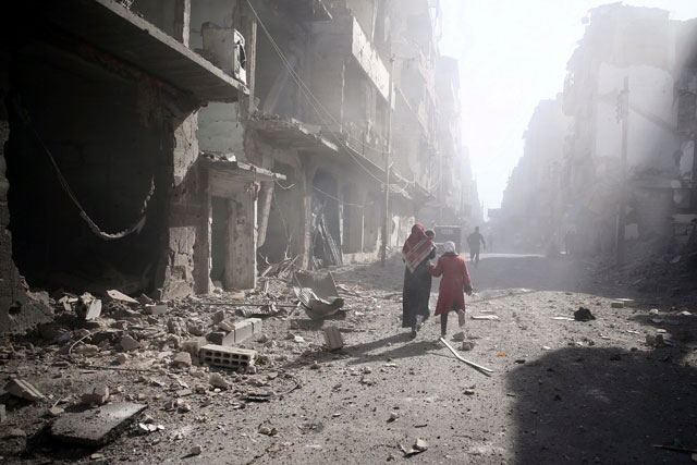 People walk past a damaged site after an air strike in the besieged rebel-held town of Douma, eastern Ghouta in Damascus, Syria, on Wednesday (Reuters photo)