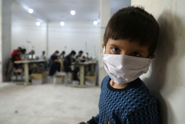A child looks on as volunteers gather in a sewing workshop to make protective face-masks in the northeastern Syrian city of Idlib (AFP photo)