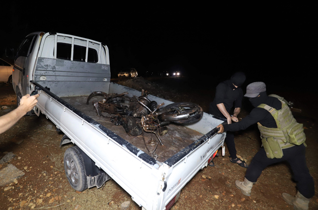 Fighters affiliated with the Hayat Tahrir Al Sham (HTS) extremist group in Syria transport the remains of a motorcycle reportedly targeted in a drone attack on the eastern edge of Syria’s rebel-held Idlib province, early on Tuesday (AFP photo)