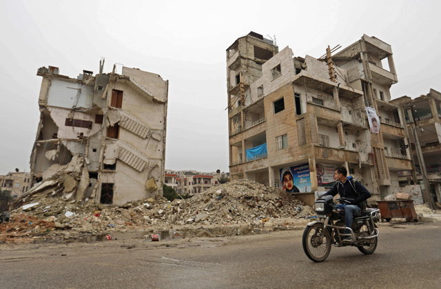 A man rides his motorcycle in front of damaged buildings in the northwestern Syrian city of Idlib on Thursday (AFP photo)