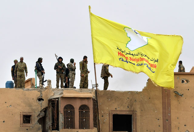 Fighters of the Syrian Democratic Forces stand atop a roof next to their unfurled flag at a position in the village of Baghouz in Syria’s eastern Deir Ezzor province near the Iraqi border on Sunday (AFP photo)
