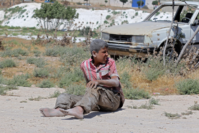A young Syrian man sits on the ground after a bombing on an industrial area of Idlib, northern Syria, on Tuesday (AFP photo)