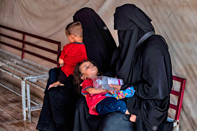 Displaced Syrian mothers hold their children as they wait outside a clinic at Al Hol camp for the internally displaced people in Al Hasakeh governorate in north-eastern Syria, on Tuesday (AFP photo)