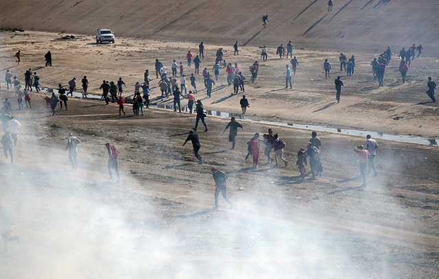 Migrants run from tear gas released by US border patrol, near the border fence between Mexico and the United States in Tijuana, Mexico, on Sunday (Reuters photo)