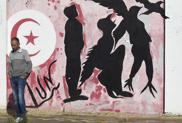 In this file photo taken on October 27, 2020, a man waits by a graffiti depicting silhouettes of a man metamorphosing into a bird symbolising freedom, in Mohamed Bouazizi Square in the centre of the town of Sidi Bouzid in central Tunisia  (AFP photo)
