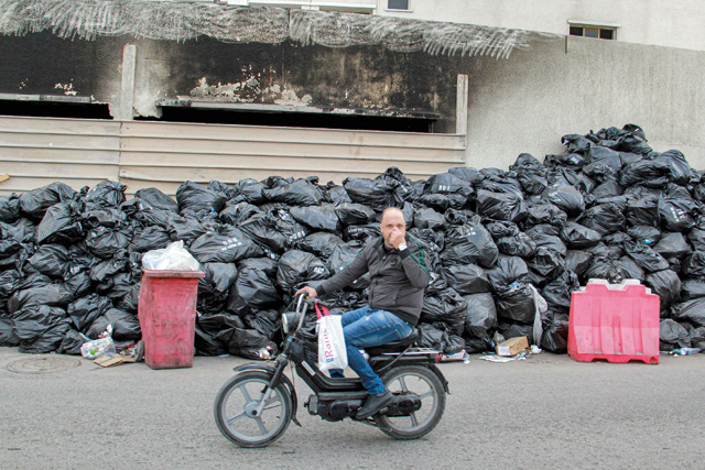 A man holds his nose while driving a motorcycle past sacks of garbage piled up along the side of a wall in the centre of the coastal city of Sfax, about 270 kilometres southeast of Tunisia’s capital, on Saturday (AFP photo)