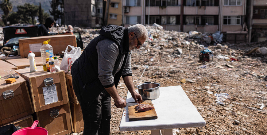 A man cuts meat at a table outdoor near his destroyed house after a 6.4-magnitude quake hit the Hatay province in southern Turkey, in Antakya, on Tuesday (AFP photo)