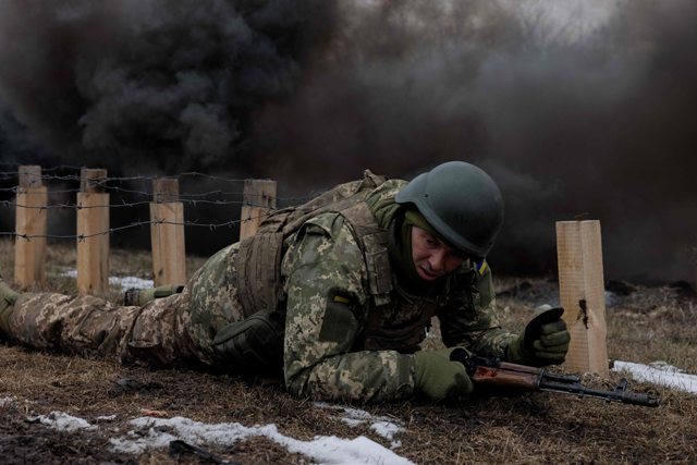 A Ukrainian serviceman of the 24th Mechanized Brigade crawls under razor wire as black smoke billows nearby, as he takes part in a training drill at an undisclosed location in the eastern region of Ukraine on March 4, 2025  (AFP photo)