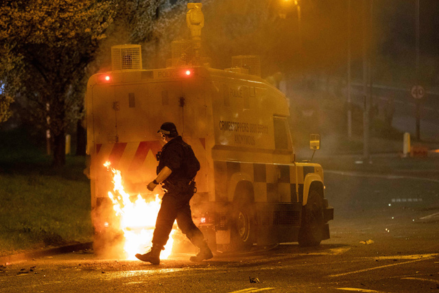 In this file photo taken on April 03, a police officer walks behind a police vehicle with flames leaping up the rear after violence broke out in Newtownabbey, north of Belfast, in Northern Ireland (AFP photo)