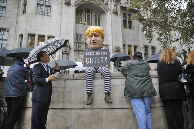 A protester wearing a mask resembling Britain's Prime Minister Boris Johnson holding a ‘guilty’ sign sits on a wall outside the supreme court in central London on Tuesday (AFP photo)