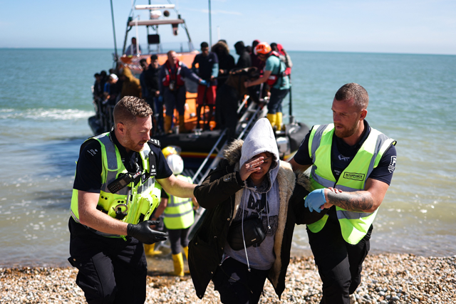 An interforce officer and a border force officer help a woman on the beach at Dungeness on the southeast coast of England, on August 16, 2023, after she disembarked from a Royal National Lifeboat Institution lifeboat after being picked up at sea with other migrants while attempting to cross the English Channel from France (AFP photo)