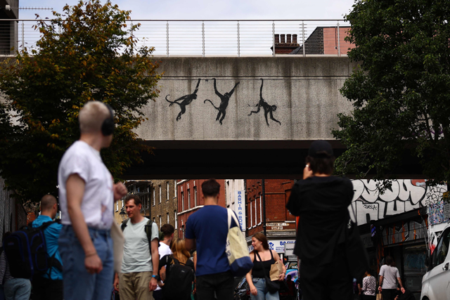 People walk past an artwork by street artist Banksy, the third to be released in three days, depicting three monkeys, painted on the side of a railway bridge in east London on Wednesday (AFP photo)