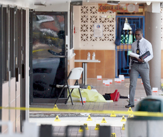 A police inspector walks near a body laying on the ground near shell case evidence markers where a mass shooting took place outside of a banquet hall on Sunday in Hialeah, Florida (AFP photo)