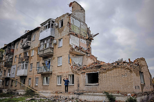 A man takes photos with a phone beside a damaged building in Lyman, Donetsk region, on Friday after the recapture of the area from the Russian forces, amid the Russian invasion of Ukraine (AFP photo)