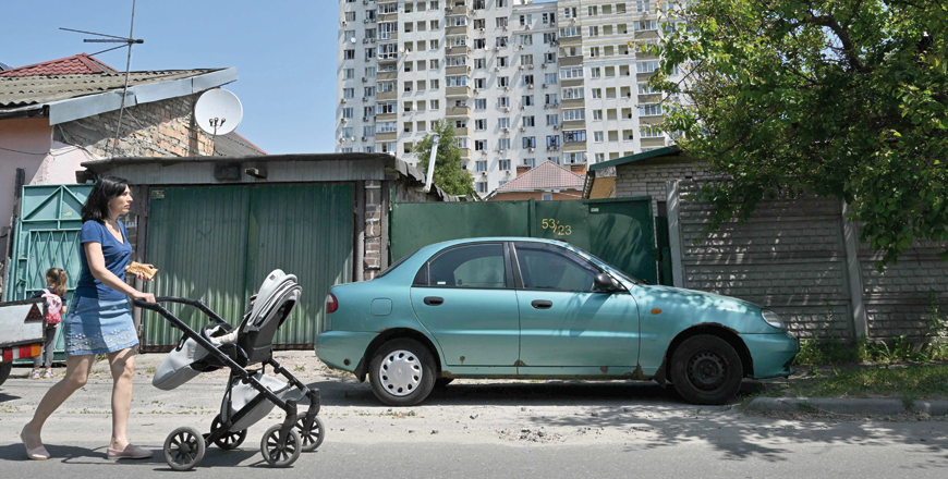 A woman pushes a pram in front of a partially destroyed building after an overnight drone attack in Kyiv on Tuesday (AFP photo)