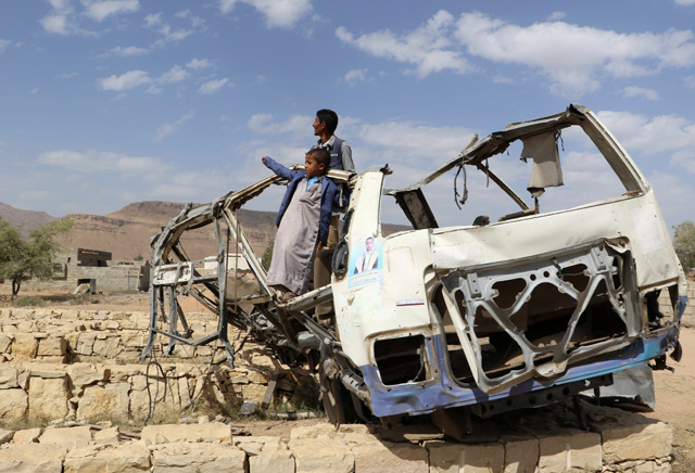 Abdullah Al Khawlani stands on Thursday with his son, Hafidh, who survived a Saudi-led air strike stand on the wreckage of a bus destroyed by the strike in Saada, Yemen (Reuters photo)
