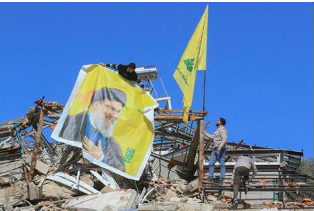 Residents hang a poster bearing a portrait of Hizbollah’s slain leader Hassan Nasrallah and the flag of the Iran-baked party on the rubble of a destroyed house in the southern border village of Adaisseh, following the Israeli army's withdrawal on February 18, 2025 
