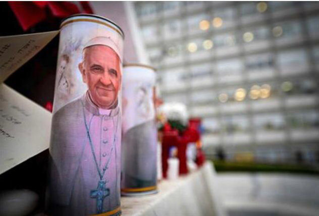 A candle with a portrait of Pope Francis is set at the bottom of a statue of Pope John Paul II outside the Gemelli hospital where Pope Francis is hospitalized for tests and treatment for bronchitis in Rome, on February 19, 2025 (AFP photo)