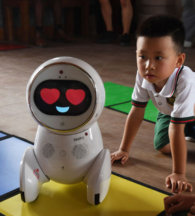 This photo taken on July 30, shows a child watching a Keeko robot make its way on a path they made from square mats at the Yiswind Institute of Multicultural Education in Beijing  (AFP photo by Greg Baker)