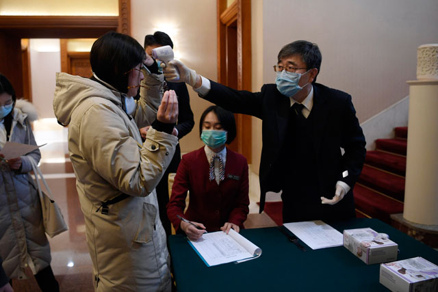A man uses a thermometer to check the temperature of a journalist to cover a meeting between World Health Organisation Director General Tedros Adhanom and Chinese State Councillor and Foreign Minister Wang Yi at the Diaoyutai State Guesthouse in Beijing on Tuesday (AFP photo)