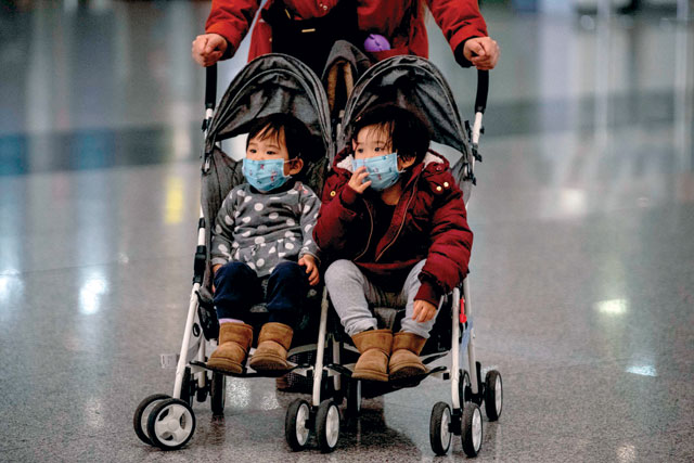 Two children wearing protective face masks sit in a buggy as they arrive at the Beijing Capital International Airport in Beijing on Sunday (AFP photo)