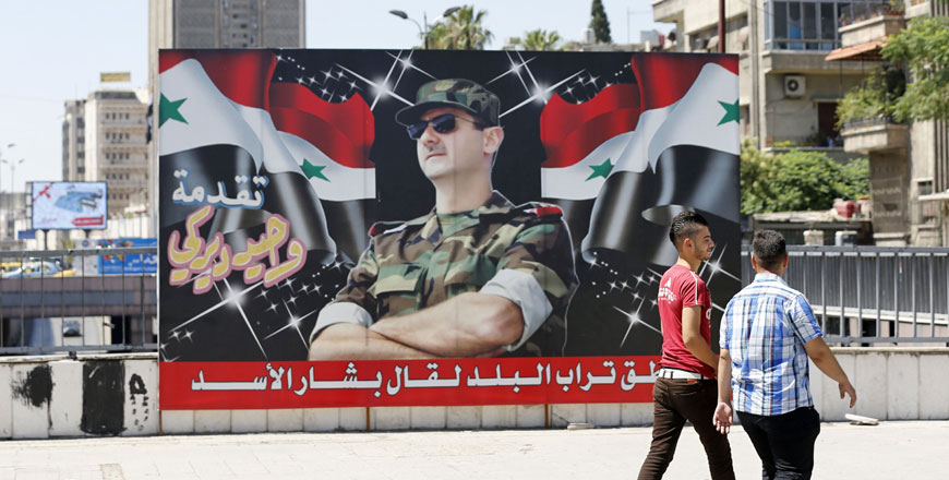 Syrian youths walk past a billboard showing a photo of Syrian President Bashar Assad on display in the centre of the capital Damascus on Monday, with a caption below reading in Arabic: ‘If the country's dust speaks, it will say Bashar Assad’  (AFP photo)