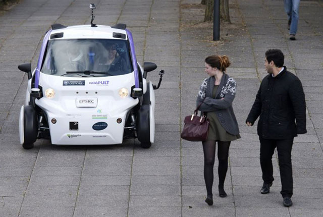 This photo shows people looking at an autonomous self-driving vehicle, as it is tested in a pedestrianised zone, during a media event in Milton Keynes, north of London, on October 11, 2016 (AFP photo by Justin Tallis)