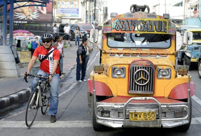 Cyclist Jack Yabut stops on his bike beside a jeepney in Manila (AFP photo)