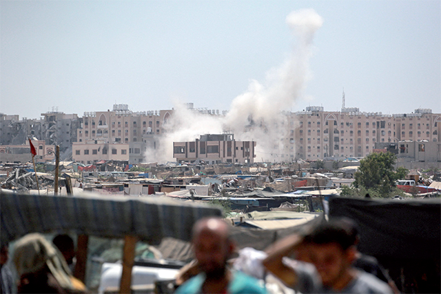 Displaced Palestinians watch from a makeshift camp as shells fired from Israeli tanks hit an area near the Hamad residential complex in Khan Yunis in the southern Gaza Strip on Sunday (AFP photo)