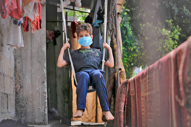 A Palestinian boy wearing a face mask due to the COVID-19 coronavirus pandemic swings at his homemade swing attached to his family door in Gaza City on Monday, during a lock down in the Palestinian enclave due to increasing cases of coronavirus infections (AFP photo)