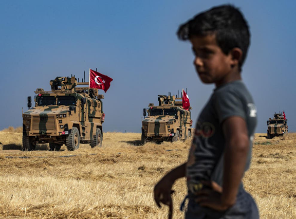 A Syrian boy watches as Turkish military vehicles, part of a US military convoy, take part in a joint patrol in the Syrian village on the outskirts of Tal Abyad town (AFP file photo)