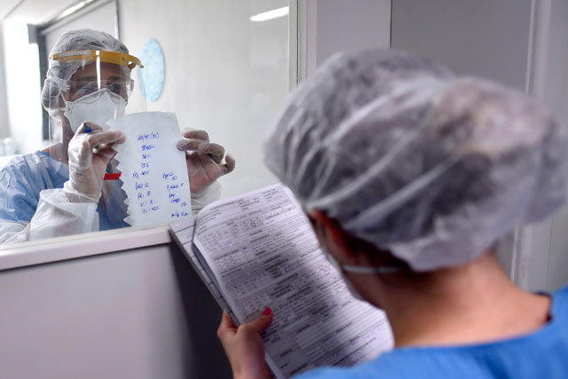 A health professional, wearing full personal protective equipment as a precautionary measure against the novel coronavirus, passes information about a COVID-19 patient through a window at the Intensive Care Unit of the Santa Casa hospital in Belo Horizonte, Brazil, on Monday (AFP photo)