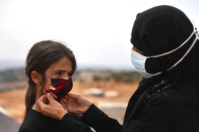 Thirty-years-old displaced Syrian woman Umm Hussein fits a face mask she sewed on the face of a child at a camp for the internally displaced people near the town of Maaret Misrin in Syria's northwestern Idlib province on Monday amid the COVID-19 pandemic crisis (AFP photo)