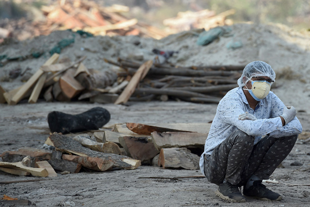 A family member sits near the funeral pyre of his loved one who died due to the COVID-19 coronavirus at a cremation ground in Allahabad on Saturday, as India recorded more than 4,000 coronavirus deaths in a day for the first time (AFP photo)