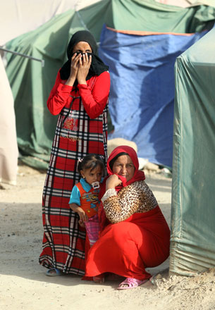 Displaced Iraqi women, who fled Ramadi, the capital of Anbar province, after it was seized by the Daesh terror group, wait outside tents at a makeshift camp for internally displaced persons in Ameriyat Al Fallujah, 30km south of Fallujah, on Sunday (AFP photo)