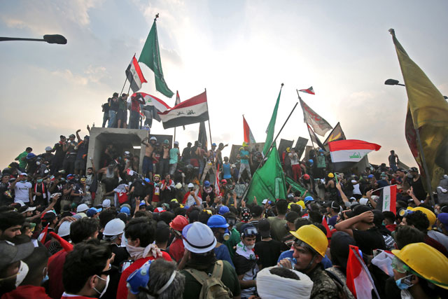 Iraqi protesters wave national flags as they stand atop concrete barriers across the capital Baghdad's Al Jumhuriya Bridge which connects between Tahrir Square and the high-security Green Zone, hosting government offices and foreign embassies, on Tuesday during the ongoing anti-government protests (AFP photo)