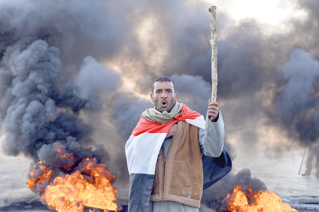 An anti-government protester draped in a national flag chants slogans while holding a stick at a make-shift roadblock with flaming tyres during a demonstration against the new Iraqi prime minister-designate in the central shiite holy shrine city of Najaf on Sunday (AFP photo)