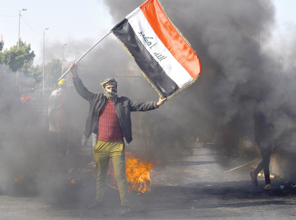 An Iraqi anti-government protester waves his national flag as others cut off a road with burning tyres in the central Shiite holy shrine city of Najaf, during a demonstration against followers of influential cleric Moqtada Sadr, on Wednesday (AFP photo)