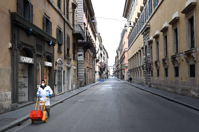 A delivery man wearing a protective mask pushes a cart across a deserted Via del Corso main shopping street in central Rome on Thursday, as Italy shut all stores except for pharmacies and food shops in a desperate bid to halt the spread of the coronavirus (AFP photo)