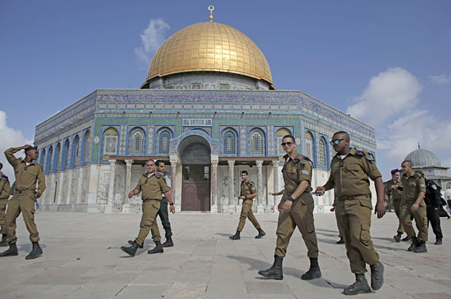 Israeli occupation soldiers walk in front of the Dome of the Rock in Jerusalem’s Al Aqsa Mosque-Al Haram Al Sharif compound, Islam’s third holiest site, as they arrive at the site under the protection of security forces on October 19, 2014 (AFP file photo) 