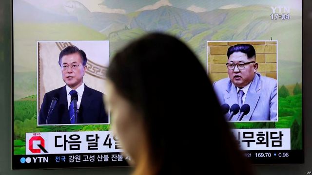  A visitor walks by a TV screen showing file footage of South Korean President Moon Jae-in, left, and North Korean leader Kim Jong Un, right, during a news program at the Seoul Railway Station in Seoul, South Korea, March 29, 2018