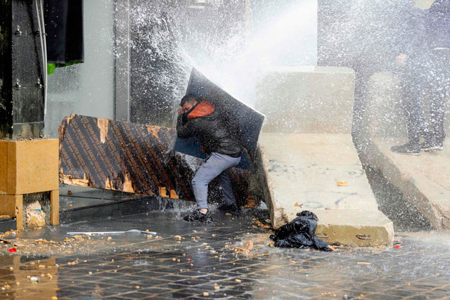 An anti-government protester uses a piece of wood to block a water cannon in central Beirut during protests on Tuesday (AFP photo)