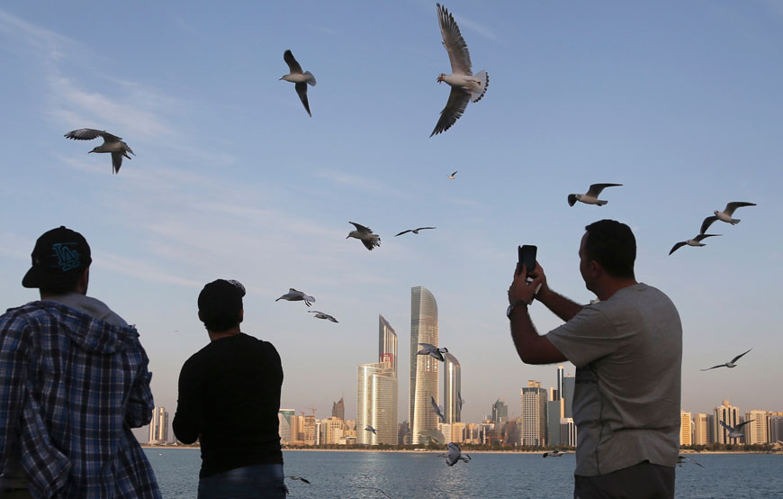 In this January 14, 2015, file photo, a man takes a photo with his mobile phone as others throw potatoe chips towards seagulls in front of city skyline in Abu Dhabi, United Arab Emirates (AP photo)