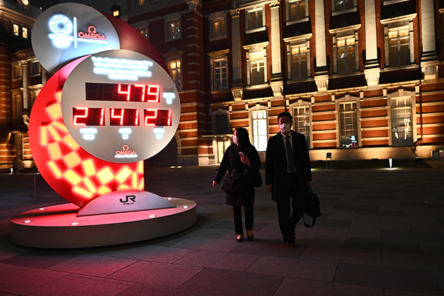 People walk past a countdown clock shows the adjusted time remaining for the postponed Tokyo Olympic Games outside Tokyo station, in Tokyo on Monday (AFP photo by Philip Fong)