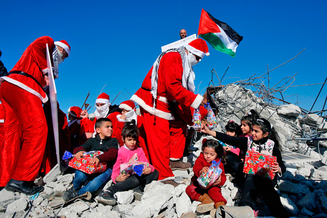 Palestinians wearing Christmas costumes distribute gifts to children seated atop the rubble of a house demolished by Israel reportedly for not being built with official licensing in the village of Al Khader, west of the biblical city of Bethlehem in the occupied West Bank, on Monday (AFP photo)